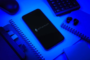 Prag, Çek Cumhuriyeti - 08 18 2025: Merkezinde Ethereum logosu bulunan bir cep telefonu ile ofis malzemeleri düzenlemesi. Ethereum merkezi olmayan uygulamalar ve kripto için bir engelleme platformudur..
