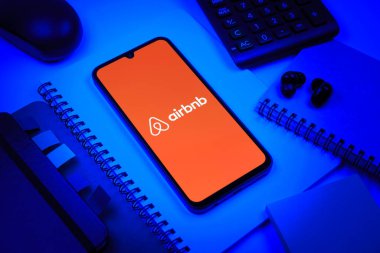 Prag, Çek Cumhuriyeti - 08 18 2025: Merkezde Airbnb logosu sergilenen bir cep telefonu ile ofis malzemeleri düzenlemesi. Airbnb dünya çapında kısa vadeli konaklama için bir platformdur..