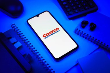 Prag, Çek Cumhuriyeti - 08 18 2025: Merkezde Costco logosunu gösteren bir cep telefonu ile ofis malzemeleri düzenlemesi. Costco toptan satış yapan bir perakendecidir. Üyelere toptan ürün satar..