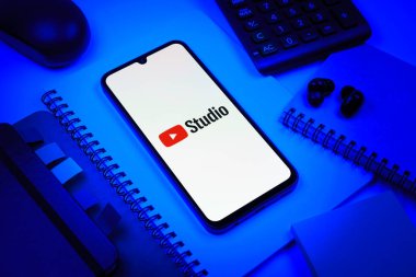 Prag, Çek Cumhuriyeti - 08 18 2025: Merkezinde Youtube Studio logosu bulunan bir cep telefonu ile ofis malzemeleri düzenlemesi. Youtube Studio YouTube kanallarını yönetmek ve analiz etmek için bir platformdur.