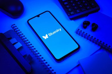 Prag, Çek Cumhuriyeti - 08 18 2025: Merkezde Bluesky logosunu gösteren bir cep telefonu ile ofis malzemeleri düzenlemesi. Bluesky merkezi olmayan ağlar için bir sosyal medya platformudur..