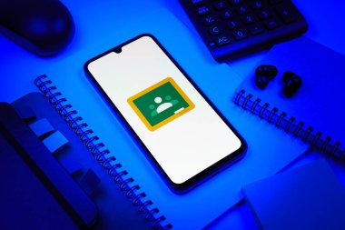 Prag, Çek Cumhuriyeti - 08 18 2025: Merkezde Google Sınıfı logosunu gösteren bir cep telefonu ile ofis malzemeleri düzenlemesi. Google Sınıfı, sınıfları ve eğitim içeriğini yönetmek için bir platformdur.