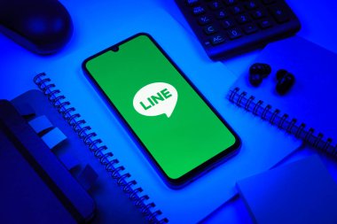 Prag, Çek Cumhuriyeti - 08 18 2025: Merkezinde hat logosu sergilenen bir cep telefonu ile ofis malzemeleri düzenlemesi. Line aramalar, mesajlar ve çokluortam paylaşımı için bir mesajlaşma uygulamasıdır.