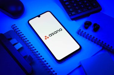 Prag, Çek Cumhuriyeti - 08 18 2025: Merkezde Asana logosunu gösteren bir cep telefonu ile ofis malzemeleri düzenlemesi. Asana görev yönetimi ve takım işbirliği için bir platformdur..