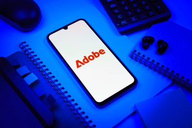 Prag, Çek Cumhuriyeti - 08 18 2025: Merkezde Adobe logosunu gösteren bir cep telefonu ile ofis malzemeleri düzenlemesi. Adobe yaratıcı araçlar ve hizmetler sunan bir yazılım şirketidir..