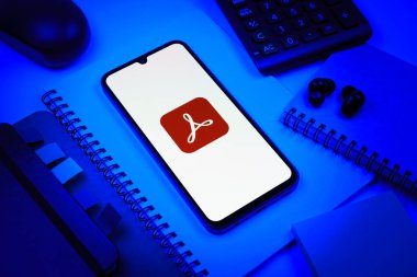 Prag, Çek Cumhuriyeti - 08 18 2025: Merkezinde Acrobat Reader logosu bulunan bir cep telefonu ile ofis malzemeleri düzenlemesi. Acrobat Reader, PDF belgelerini görüntülemek ve yönetmek için bir platformdur.