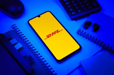Prag, Çek Cumhuriyeti - 08 18 2025: Merkezde DHL logosu sergilenen bir cep telefonu ile ofis malzemeleri düzenlemesi. DHL uluslararası nakliye hizmeti sunan bir lojistik şirketidir..