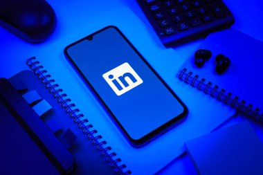 Prag, Çek Cumhuriyeti - 08 18 2025: Merkezde LinkedIn logosunu gösteren bir cep telefonu ile ofis malzemeleri düzenlemesi. LinkedIn, insanları ve şirketleri birbirine bağlayan profesyonel bir ağ..