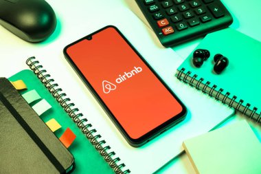 Prag, Çek Cumhuriyeti - 08 18 2025: Merkezde Airbnb logosu sergilenen bir cep telefonu ile ofis malzemeleri düzenlemesi. Airbnb dünya çapında kısa vadeli konaklama için bir platformdur..