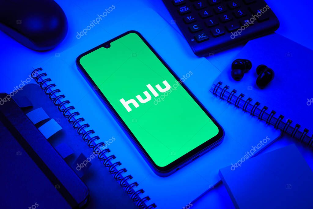 Prague, Czechia - 08 18 2025: An arrangement of office supplies with a mobile phone in the center displaying Hulu logo. Hulu is a streaming platform for TV shows, movies, and live TV.