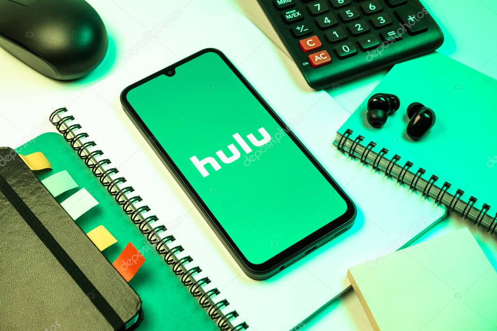 Prague, Czechia - 08 18 2025: An arrangement of office supplies with a mobile phone in the center displaying Hulu logo. Hulu is a streaming platform for TV shows, movies, and live TV.