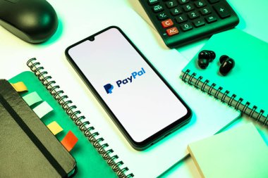 Prag, Çek Cumhuriyeti - 08 18 2025: Merkezde PayPal logosunu gösteren bir cep telefonu ile ofis malzemeleri düzenlemesi. PayPal çevrimiçi ödemeler ve para transferleri için bir platformdur.