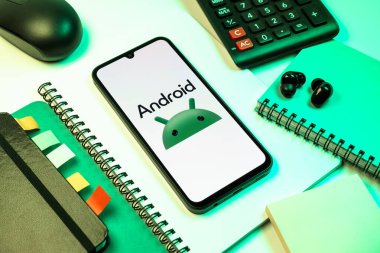 Prag, Çek Cumhuriyeti - 08 18 2025: Merkezde Android logosunu gösteren bir cep telefonu ile ofis malzemeleri düzenlemesi. Android akıllı telefonlar ve tabletler için mobil bir işletim sistemidir..