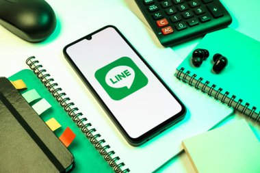 Prag, Çek Cumhuriyeti - 08 18 2025: Merkezinde hat logosu sergilenen bir cep telefonu ile ofis malzemeleri düzenlemesi. Line aramalar, mesajlar ve çokluortam paylaşımı için bir mesajlaşma uygulamasıdır.