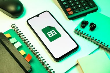 Prag, Çek Cumhuriyeti - 08 18 2025: Merkezde Google Sheets logosunu gösteren bir cep telefonu ile ofis malzemeleri düzenlemesi. Google Sayfalar tablo oluşturmak ve yönetmek için bir platformdur.