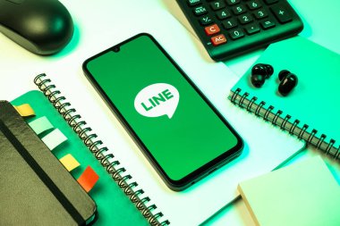Prag, Çek Cumhuriyeti - 08 18 2025: Merkezinde hat logosu sergilenen bir cep telefonu ile ofis malzemeleri düzenlemesi. Line aramalar, mesajlar ve çokluortam paylaşımı için bir mesajlaşma uygulamasıdır.