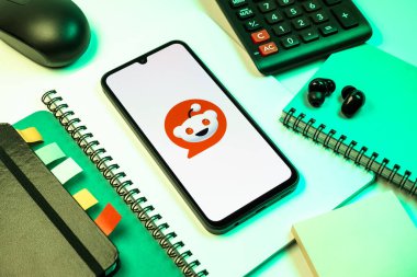 Prag, Çek Cumhuriyeti - 08 18 2025: Merkezde Reddit logosunu gösteren bir cep telefonu ile ofis malzemeleri düzenlemesi. Reddit tartışma, haber ve toplum içeriği için bir platformdur.