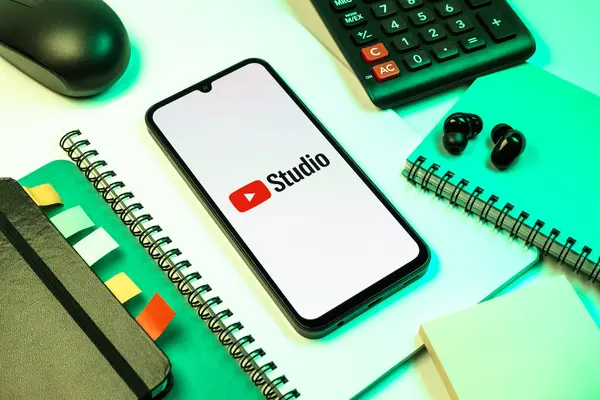 Prag, Çek Cumhuriyeti - 08 18 2025: Merkezinde Youtube Studio logosu bulunan bir cep telefonu ile ofis malzemeleri düzenlemesi. Youtube Studio YouTube kanallarını yönetmek ve analiz etmek için bir platformdur.