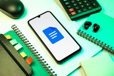 Prag, Çek Cumhuriyeti - 08 18 2025: Merkezde Google Docs logosunu gösteren bir cep telefonu ile ofis malzemeleri düzenlemesi. Google Docs metin belgeleri oluşturmak ve düzenlemek için bir platformdur.
