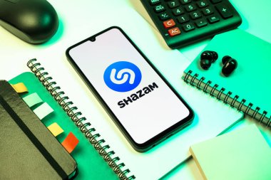 Prag, Çek Cumhuriyeti - 08 18 2025: Merkezinde Shazam logosu bulunan bir cep telefonu ile ofis malzemeleri düzenlemesi. Shazam şarkıları ve müzik parçalarını tanımlamak için bir uygulamadır.