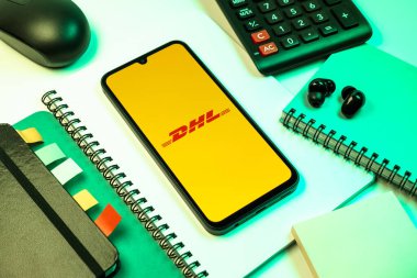 Prag, Çek Cumhuriyeti - 08 18 2025: Merkezde DHL logosu sergilenen bir cep telefonu ile ofis malzemeleri düzenlemesi. DHL uluslararası nakliye hizmeti sunan bir lojistik şirketidir..