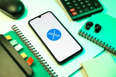 Prag, Çek Cumhuriyeti - 08 18 2025: Merkezinde X logosu sergilenen bir cep telefonu ile ofis malzemeleri düzenlemesi. X, kısa gönderileri ve güncellemeleri paylaşmak için bir platformdur.