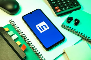 Prag, Çek Cumhuriyeti - 08 18 2025: Merkezde LinkedIn logosunu gösteren bir cep telefonu ile ofis malzemeleri düzenlemesi. LinkedIn, insanları ve şirketleri birbirine bağlayan profesyonel bir ağ..