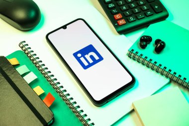 Prag, Çek Cumhuriyeti - 08 18 2025: Merkezde LinkedIn logosunu gösteren bir cep telefonu ile ofis malzemeleri düzenlemesi. LinkedIn, insanları ve şirketleri birbirine bağlayan profesyonel bir ağ..