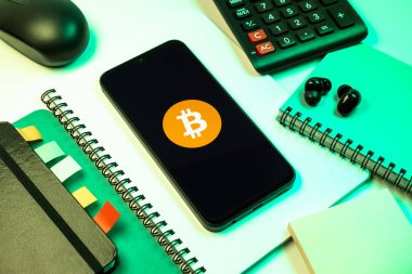 Prag, Çek Cumhuriyeti - 08 18 2025: Merkezde Bitcoin logosu sergilenen bir cep telefonu ile ofis malzemeleri düzenlemesi. Bitcoin merkezi olmayan işlemler için dijital bir kripto para birimidir.