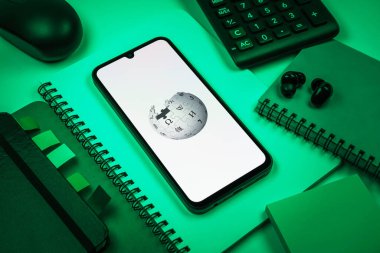 Prag, Çek Cumhuriyeti - 08 18 2025: Merkezinde Wikipedia logosu bulunan bir cep telefonu ile ofis malzemeleri düzenlemesi. Vikipedi çevrimiçi bir ansiklopedidir..