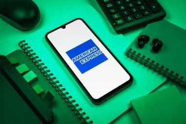 Prag, Çek Cumhuriyeti - 08 18 2025: Merkezde American Express logosunu gösteren bir cep telefonu ile ofis malzemeleri düzenlemesi. American Express kart ve bankacılık sunan bir finans şirketidir..