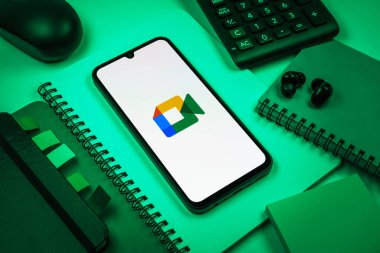 Prag, Çek Cumhuriyeti - 08 18 2025: Merkezde Google Meet logosunu gösteren bir cep telefonu ile ofis malzemeleri düzenlemesi. Google Meet video toplantıları ve çevrimiçi işbirliği için bir platformdur.