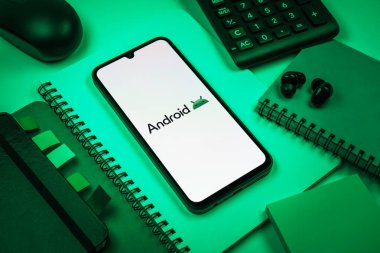 Prag, Çek Cumhuriyeti - 08 18 2025: Merkezde Android logosunu gösteren bir cep telefonu ile ofis malzemeleri düzenlemesi. Android akıllı telefonlar ve tabletler için mobil bir işletim sistemidir..