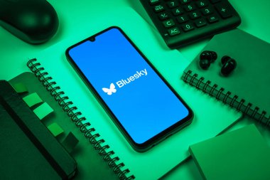 Prag, Çek Cumhuriyeti - 08 18 2025: Merkezde Bluesky logosunu gösteren bir cep telefonu ile ofis malzemeleri düzenlemesi. Bluesky merkezi olmayan ağlar için bir sosyal medya platformudur..