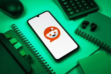 Prag, Çek Cumhuriyeti - 08 18 2025: Merkezde Reddit logosunu gösteren bir cep telefonu ile ofis malzemeleri düzenlemesi. Reddit tartışma, haber ve toplum içeriği için bir platformdur.