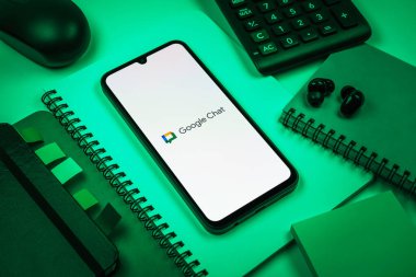 Prag, Çek Cumhuriyeti - 08 18 2025: Merkezde Google Chat logosunu gösteren bir cep telefonu ile ofis malzemeleri düzenlemesi. Google Chat mesajlaşma ve takım işbirliği için bir platformdur.