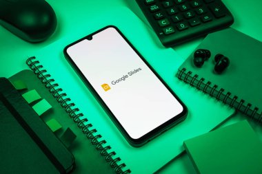 Prag, Çek Cumhuriyeti - 08 18 2025: Merkezde Google Slides logosunu gösteren bir cep telefonu ile ofis malzemeleri düzenlemesi. Google Slides sunumlar ve slayt gösterileri oluşturmak için bir platformdur.