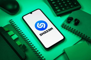 Prag, Çek Cumhuriyeti - 08 18 2025: Merkezinde Shazam logosu bulunan bir cep telefonu ile ofis malzemeleri düzenlemesi. Shazam şarkıları ve müzik parçalarını tanımlamak için bir uygulamadır.
