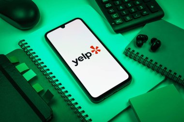 Prag, Çek Cumhuriyeti - 08 18 2025: Merkezde Yelp logosu sergilenen bir cep telefonu ile ofis malzemeleri düzenlemesi. Yelp yerel işletmeleri bulmak ve incelemek için bir platformdur.