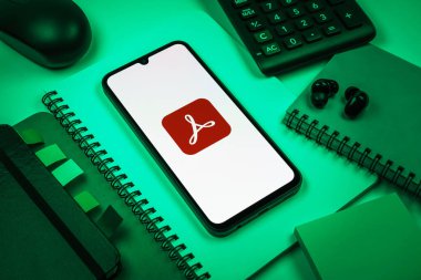 Prag, Çek Cumhuriyeti - 08 18 2025: Merkezinde Acrobat Reader logosu bulunan bir cep telefonu ile ofis malzemeleri düzenlemesi. Acrobat Reader, PDF belgelerini görüntülemek ve yönetmek için bir platformdur.