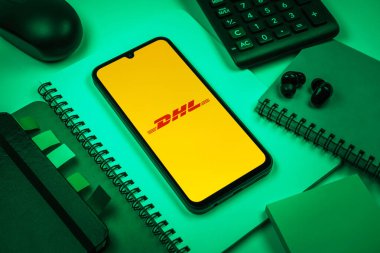 Prag, Çek Cumhuriyeti - 08 18 2025: Merkezde DHL logosu sergilenen bir cep telefonu ile ofis malzemeleri düzenlemesi. DHL uluslararası nakliye hizmeti sunan bir lojistik şirketidir..