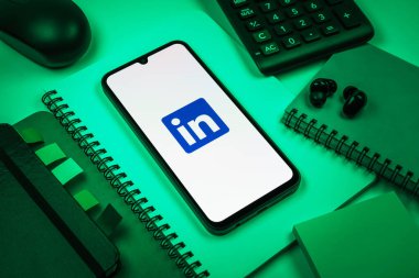 Prag, Çek Cumhuriyeti - 08 18 2025: Merkezde LinkedIn logosunu gösteren bir cep telefonu ile ofis malzemeleri düzenlemesi. LinkedIn, insanları ve şirketleri birbirine bağlayan profesyonel bir ağ..