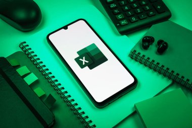 Prag, Çek Cumhuriyeti - 08 18 2025: Excel logosu sergilenen bir cep telefonu ile ofis malzemeleri düzenlemesi. Excel, tablo, veri analizi ve hesaplamalar için bir yazılımdır..