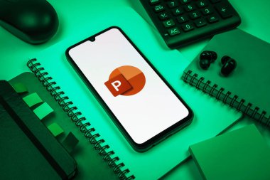 Prag, Çek Cumhuriyeti - 08 18 2025: Merkezde Powerpoint logosunu gösteren bir cep telefonu ile ofis malzemeleri düzenlemesi. Powerpoint sunumlar ve slayt gösterileri oluşturmak için bir yazılımdır..