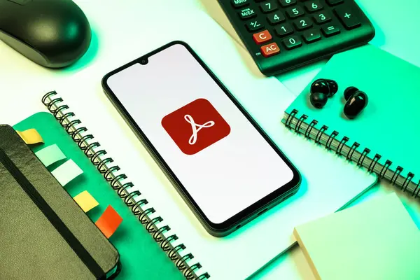 Prag, Çek Cumhuriyeti - 08 18 2025: Merkezinde Acrobat Reader logosu bulunan bir cep telefonu ile ofis malzemeleri düzenlemesi. Acrobat Reader, PDF belgelerini görüntülemek ve yönetmek için bir platformdur.