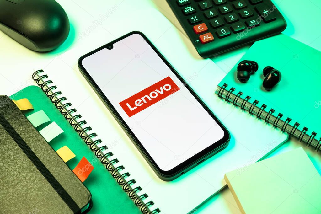 Prague, Czechia - 08 18 2025: An arrangement of office supplies with a mobile phone in the center displaying Lenovo logo. Lenovo is a technology company producing computers and electronics.