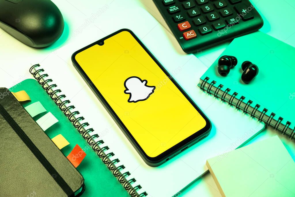 Prague, Czechia - 08 18 2025: An arrangement of office supplies with a mobile phone in the center displaying Snapchat logo. Snapchat is an app for sending photos, videos, and temporary messages.