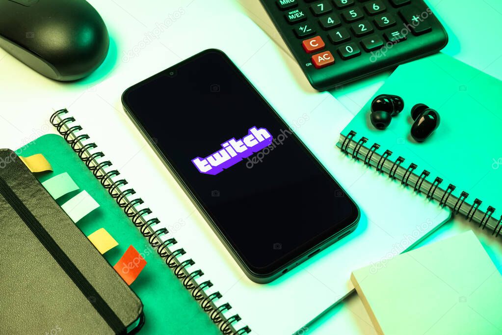 Prague, Czechia - 08 18 2025: An arrangement of office supplies with a mobile phone in the center displaying Twitch logo. Twitch is a platform for live streaming games and content.
