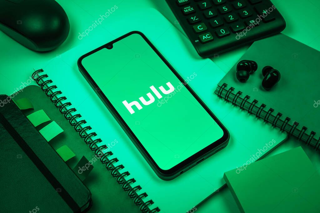 Prague, Czechia - 08 18 2025: An arrangement of office supplies with a mobile phone in the center displaying Hulu logo. Hulu is a streaming platform for TV shows, movies, and live TV.