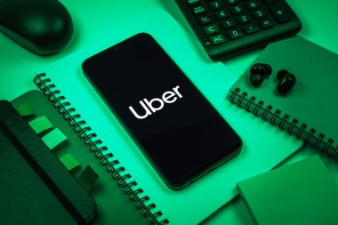 Prag, Çek Cumhuriyeti - 08 18 2025: Merkezde Uber logosu gösteren bir cep telefonu ile ofis malzemeleri düzenlemesi. Uber ulaşım ve dağıtım hizmetleri için bir gezinti selamlama uygulaması.